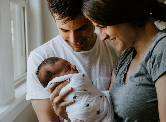 Pareja sosteniendo a su bebé recién nacido junto a una ventana